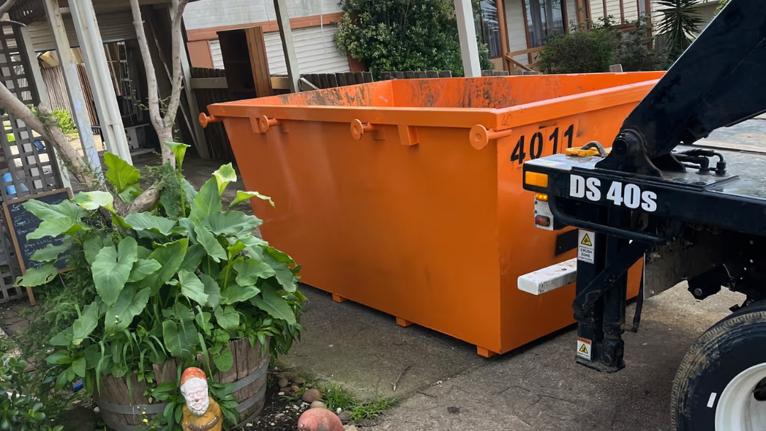 An orange metal dumpster container with the number 4011 on the side, parked outdoors on a concrete driveway next to a black vehicle on a residential street.